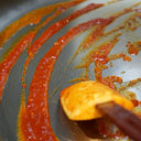 Fresh chilli sauce being scraped across the pan with a spatula, showing its thick, natural texture