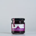 A glass jar of The Mulberry Pigs Apple & Black Currant Jam with a black lid and a purple label, set against a plain light gray background.