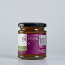 A glass jar of Apple and thyme butter  with a black lid and a purple label, photographed on a clean light gray background.