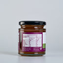 A glass jar of Apple and thyme butter  with a black lid, showing the back label with nutrition information, photographed against a light gray background.