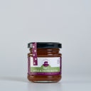 A glass jar of The Mulberry Pig Apple & Thyme Butter with a black lid and a purple and green label, set against a plain light gray background.