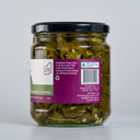 A glass jar of The Mulberry Pig Pickled Jalapeños with a black lid and a white, dark green, and purple label showing the blurb, set against a plain light grey background.