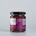 A glass jar of The Mulberry Pig Quince Paste, showing the back of the label with product details, set against a clean light gray background.