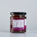 A glass jar of Quince Paste with a black lid and a purple nutrition label, shown from the back on a light gray background.