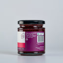 A glass jar of The Mulberry pig Raspberry Jam , showing the back of the label with product details, set against a clean light gray background.