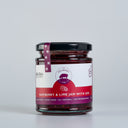 A glass jar of Raspberry & Lime Jam with Gin by The Mulberry Pig, featuring a white and red label with a black lid and a purple seal ribbon, set against a plain light gray background.