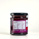 A glass jar of The Mulberry Pig, Raspberry & Lime Jam with Gin with a black lid, showing the back of the label with nutrition information. The jar is set against a clean, light gray background.
