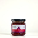 A glass jar of The Mulberry Pig, Raspberry & Lime Jam with Gin, featuring a black lid and a white and red label, set against a plain light gray background.