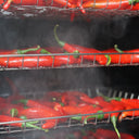 Red chili peppers being naturally smoked on metal racks inside a smoking chamber with visible smoke.