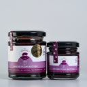 Two glass jars of  Spiced Plum Butter by The Mulberry Pig, one large and one small, with black lids and purple labels, set against a light gray background.