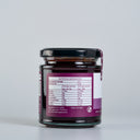 A glass jar of Spiced Plum Butter with a black lid, showing the back of the label with nutrition information. The jar is set against a clean, light gray background.