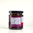 A glass jar of The Mulberry Pig Strawberry and Cinnamon Jam, showing the back label with nutrition information, on a white background.
