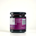 A glass jar of The Mulberry Pig Apple and Blackcurrant jam showing the back of the label with product details, set against a clean light gray background.