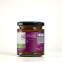 A glass jar of Apple and thyme butter  with a black lid and a purple label, photographed on a clean light cream background.