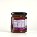 A glass jar of Apple and thyme butter  with a black lid, showing the back label with nutrition information, photographed against a cream background.