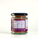 A glass jar of The Mulberry Pig Smoked Chilli Garlic Salt with a black lid and a white and pink label with the nutrition panel on show, set against a plain cream background.