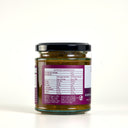 A glass jar of The Mulberry Pig Eggplant, Sultana & Curry Leaf Chutney with a black lid and a purple and white label, with the nutritional panel on show,  set against a plain white background.