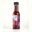 A bottle of Mulberry Pig Slow Smoke Hot Sauce on a clean white background. The glass bottle shows the reddish-brown sauce inside, featuring a white and red label with a purple brand logo and a black cap, showing the made in WA logo on the label