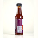 A bottle of Mulberry Pig Slow Smoke Hot Sauce on a clean white background. The glass bottle shows the reddish-brown sauce inside, featuring a white and red label with a purple brand logo and a black cap, with nutrition panel showing 