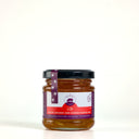 A glass jar of Blood Orange and Ginger Marmalade with a black lid and a purple and white label, set against a plain light gray background.