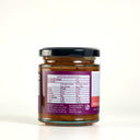A glass jar of The Mulberry Pig Peach, Chilli and Black Pepper Chutney on a clean white background. The jar has a black lid, a purple and white label showing nutritional info, and a purple seal ribbon, with visible chunks of reddish-brown chutney inside.