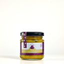 A small glass jar of Piccalilli by The Mulberry Pig, featuring a black lid and a white, yellow, and purple label, set against a plain white background.
