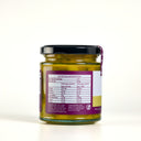 A glass jar of Piccalilli by The Mulberry Pig, featuring a black lid and a white, yellow, and purple label showing the nutritional label, set against a plain white background.