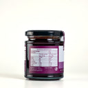 A glass jar of Spiced Plum Butter with a black lid, showing the back of the label with nutrition information. The jar is set against a clean, light gray background.