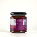 A glass jar of The Mulberry Pig Quince Paste, showing the back of the label with product details, set against a clean light cream background.