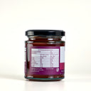 A glass jar of Quince Paste with a black lid and a purple nutrition label, shown from the back on a light cream background.