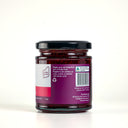A glass jar of The Mulberry pig Raspberry Jam , showing the back of the label with product details, set against a clean light gray background.